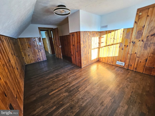 bonus room featuring lofted ceiling, dark wood-type flooring, wooden walls, and a textured ceiling