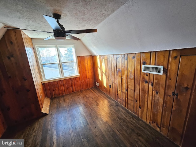 bonus room featuring lofted ceiling, ceiling fan, dark hardwood / wood-style floors, a textured ceiling, and wood walls