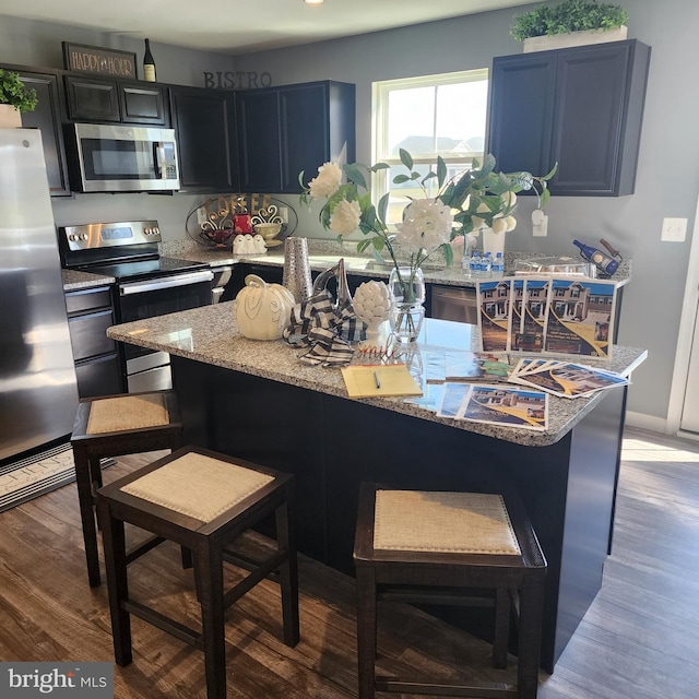 kitchen with stainless steel appliances, wood-type flooring, a breakfast bar area, and light stone counters