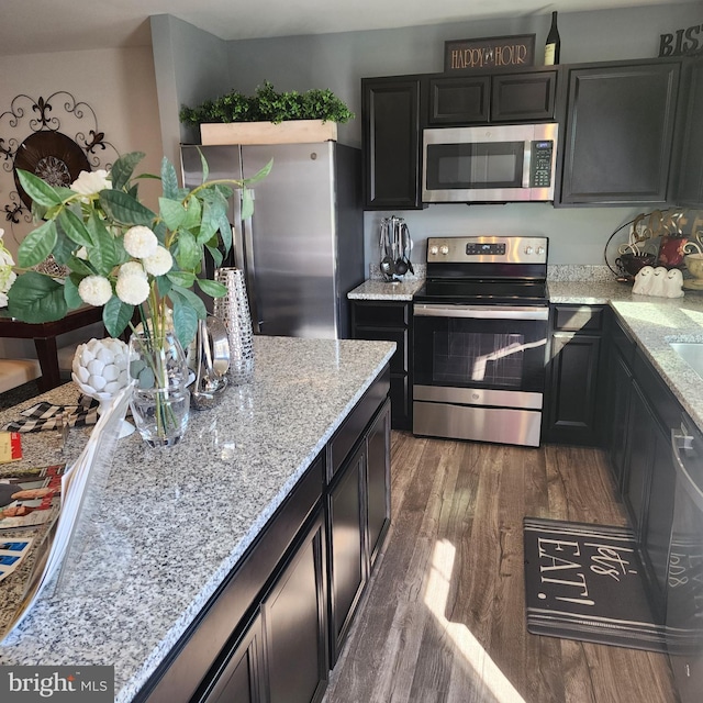 kitchen with dark wood-type flooring, stainless steel appliances, and light stone countertops