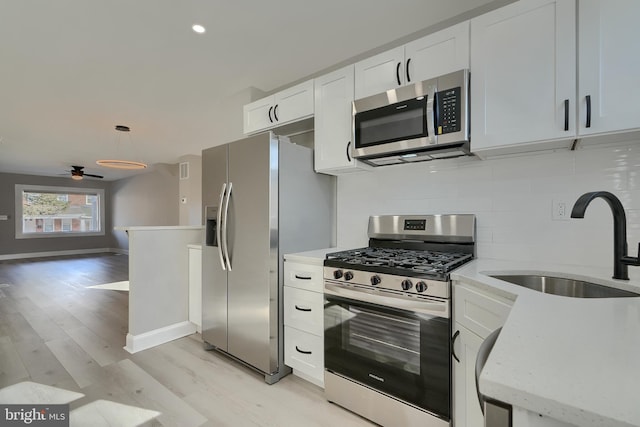 kitchen featuring sink, appliances with stainless steel finishes, white cabinetry, backsplash, and decorative light fixtures