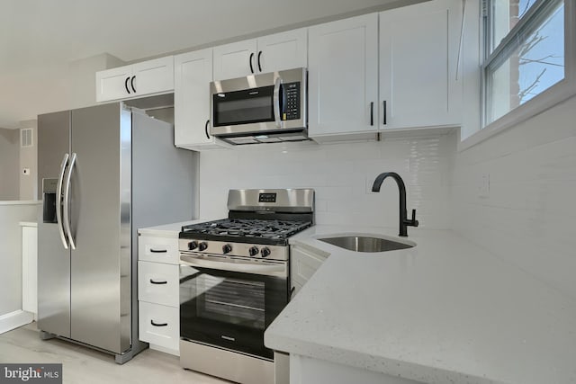 kitchen with sink, white cabinetry, light stone counters, stainless steel appliances, and decorative backsplash