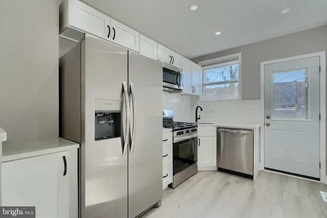 kitchen featuring sink, white cabinetry, light wood-type flooring, stainless steel appliances, and backsplash