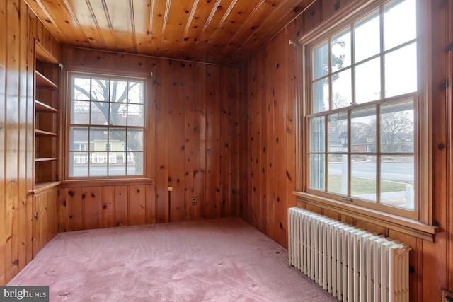 carpeted empty room featuring a healthy amount of sunlight, radiator heating unit, wooden ceiling, and wood walls