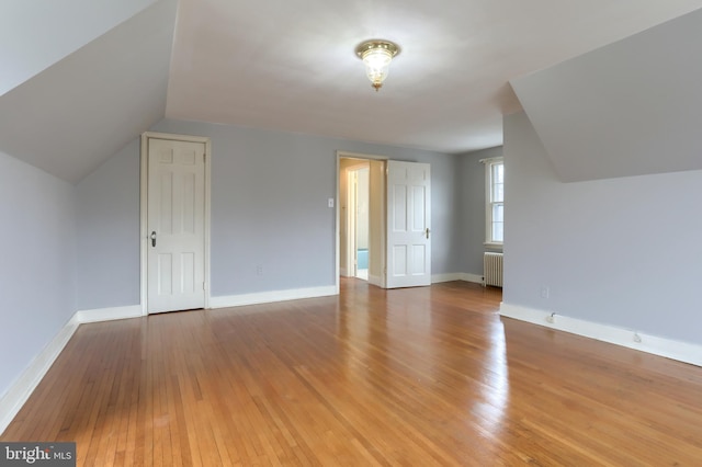 additional living space with hardwood / wood-style flooring, radiator heating unit, and vaulted ceiling