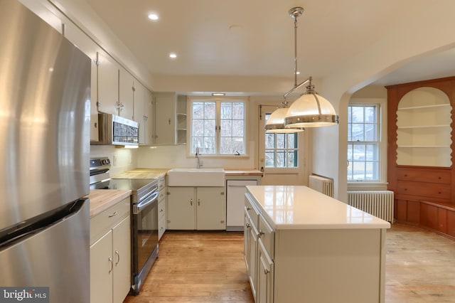 kitchen with appliances with stainless steel finishes, radiator heating unit, white cabinetry, sink, and hanging light fixtures