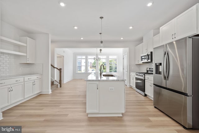 kitchen featuring sink, appliances with stainless steel finishes, hanging light fixtures, white cabinets, and a center island with sink