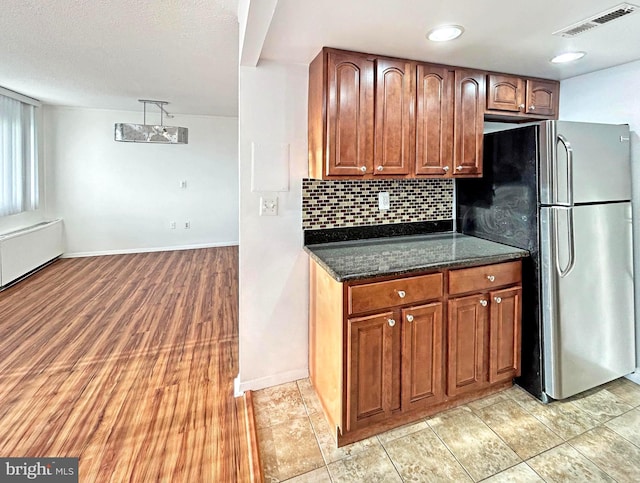 kitchen with tasteful backsplash, visible vents, brown cabinetry, freestanding refrigerator, and dark stone countertops