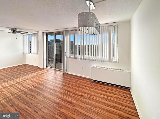 empty room with radiator heating unit, a textured ceiling, baseboards, and wood finished floors