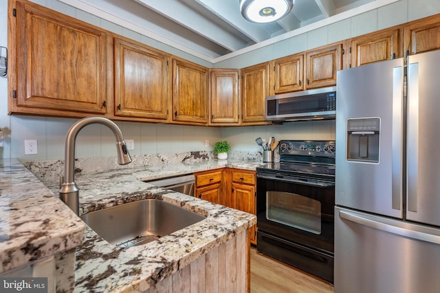 kitchen with appliances with stainless steel finishes, light stone countertops, sink, and light wood-type flooring