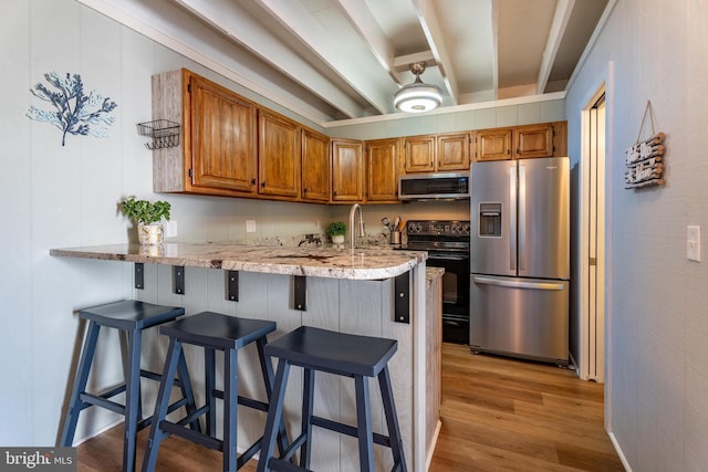 kitchen featuring appliances with stainless steel finishes, a kitchen bar, kitchen peninsula, beamed ceiling, and light wood-type flooring