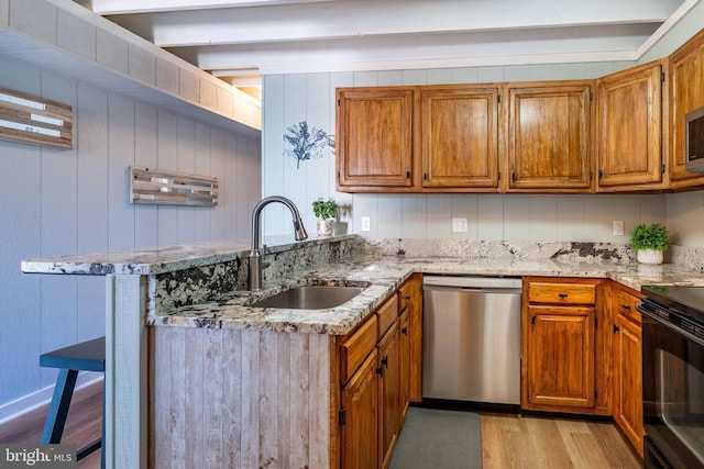 kitchen with stainless steel appliances, light stone countertops, sink, and light hardwood / wood-style floors