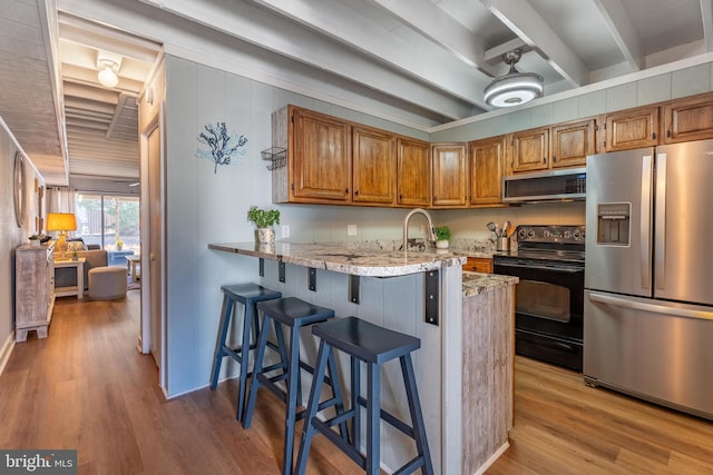 kitchen with appliances with stainless steel finishes, sink, kitchen peninsula, beam ceiling, and light hardwood / wood-style flooring