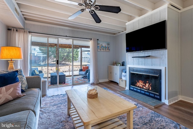 living room featuring hardwood / wood-style flooring, ceiling fan, a tiled fireplace, and beamed ceiling