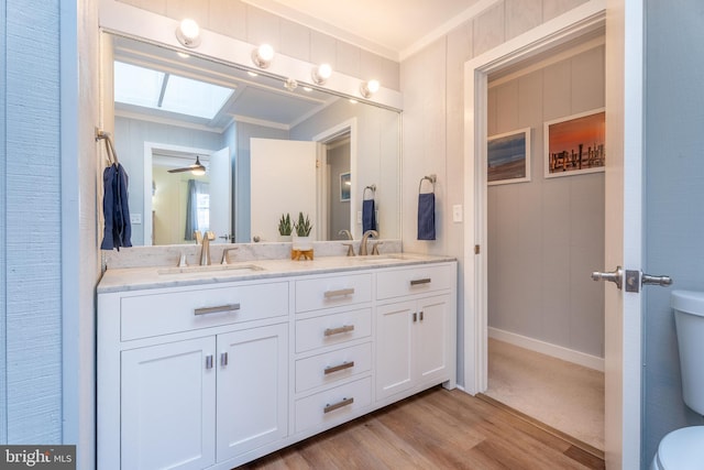 bathroom featuring a skylight, wood-type flooring, vanity, ornamental molding, and toilet