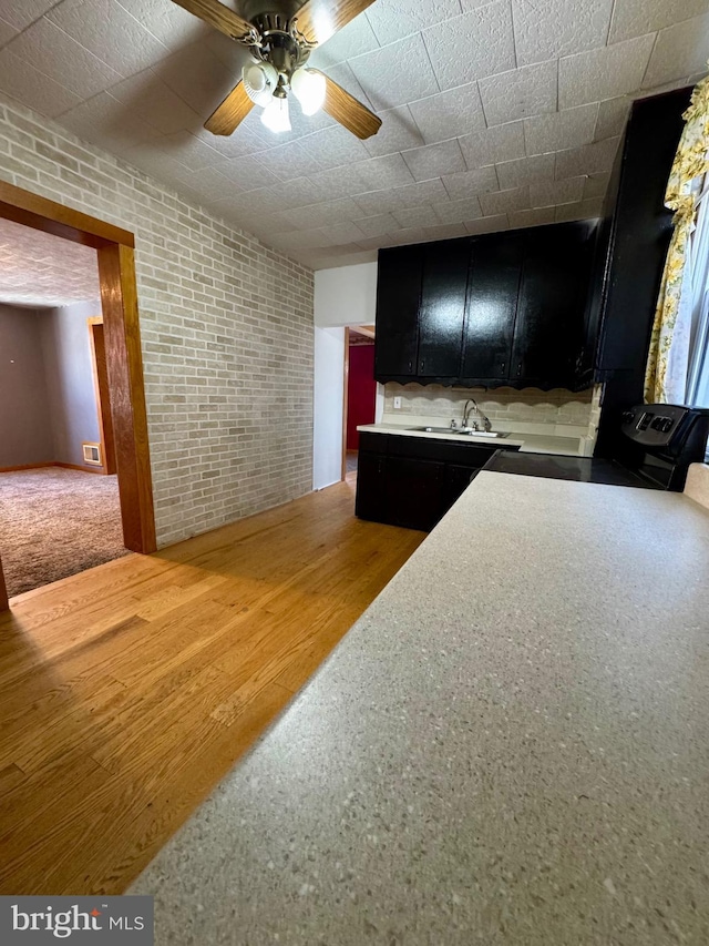 kitchen with brick wall, sink, hardwood / wood-style floors, and ceiling fan