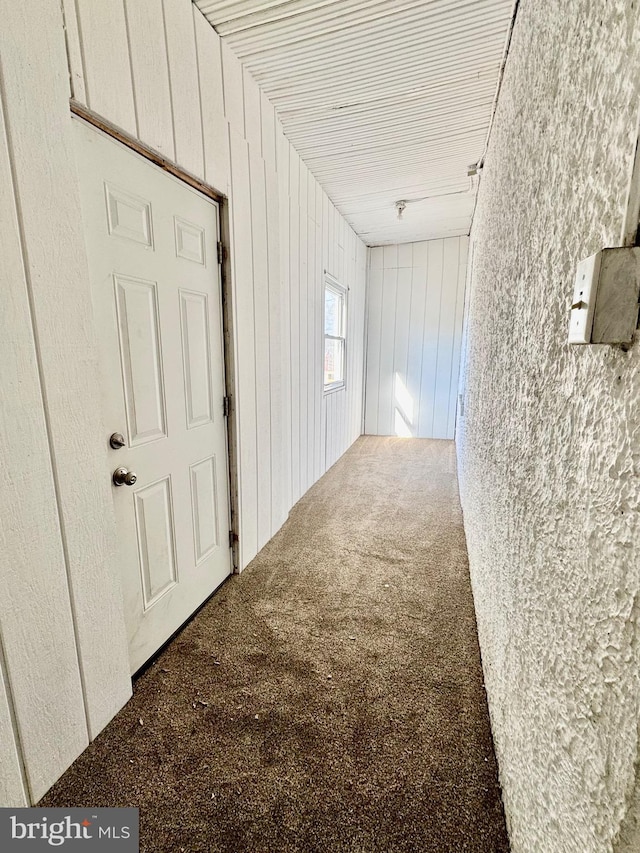 hallway with dark colored carpet and wood walls