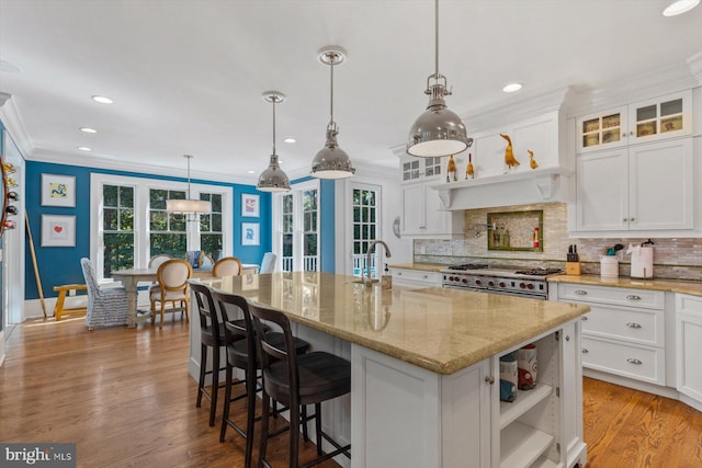 kitchen with light stone counters, double oven range, pendant lighting, a kitchen island with sink, and white cabinets