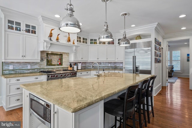 kitchen with built in appliances, white cabinets, and a center island with sink