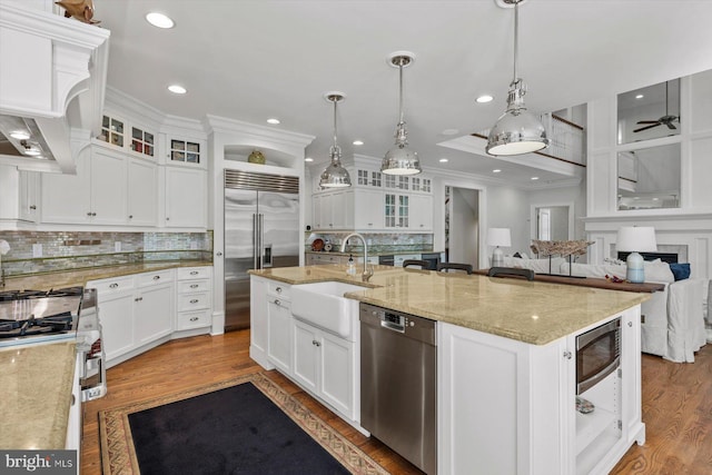 kitchen with decorative light fixtures, high quality appliances, white cabinetry, a kitchen island with sink, and light stone countertops