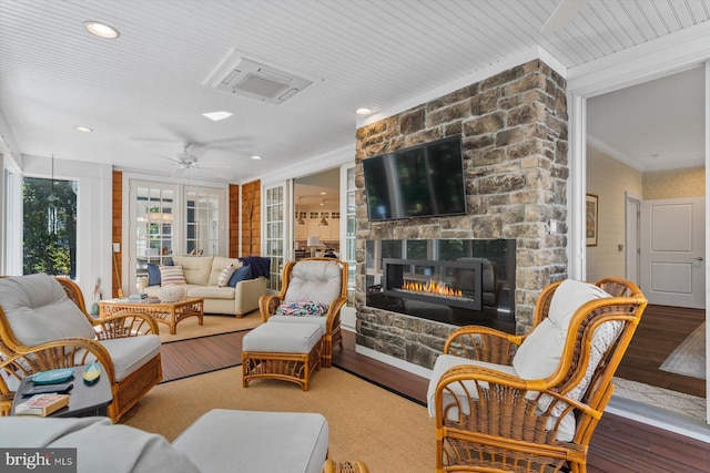 living room with crown molding, a stone fireplace, and hardwood / wood-style flooring