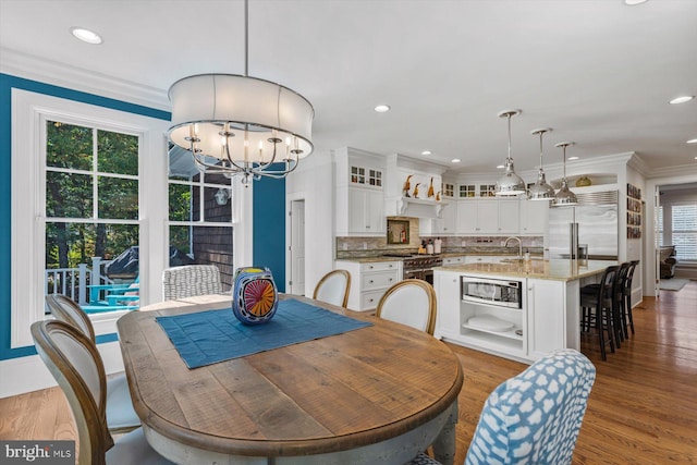 dining space featuring an inviting chandelier, sink, crown molding, and dark wood-type flooring