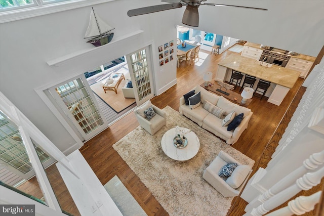 living room with wood-type flooring, plenty of natural light, a towering ceiling, and ceiling fan