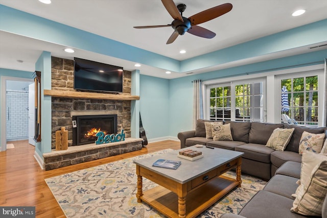 living room with a stone fireplace, light hardwood / wood-style floors, and ceiling fan