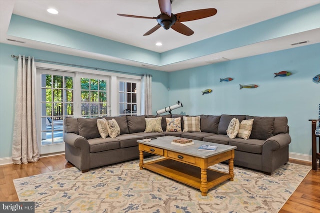 living room featuring hardwood / wood-style floors, a raised ceiling, and ceiling fan