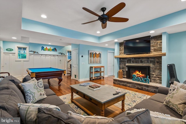 living room featuring a stone fireplace, wood-type flooring, pool table, ceiling fan, and a raised ceiling