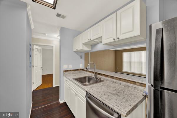 kitchen featuring appliances with stainless steel finishes, white cabinetry, a sink, and light stone countertops