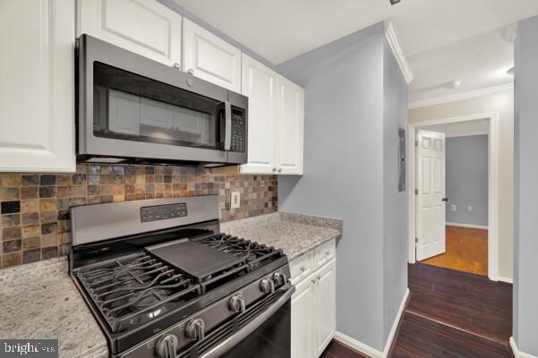 kitchen with light stone counters, appliances with stainless steel finishes, dark wood-type flooring, and white cabinetry