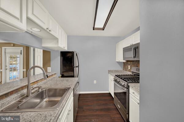 kitchen featuring dark wood-style flooring, a sink, white cabinets, appliances with stainless steel finishes, and decorative backsplash