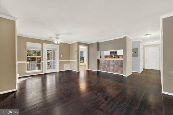 unfurnished living room featuring crown molding, ceiling fan, dark wood-type flooring, and baseboards