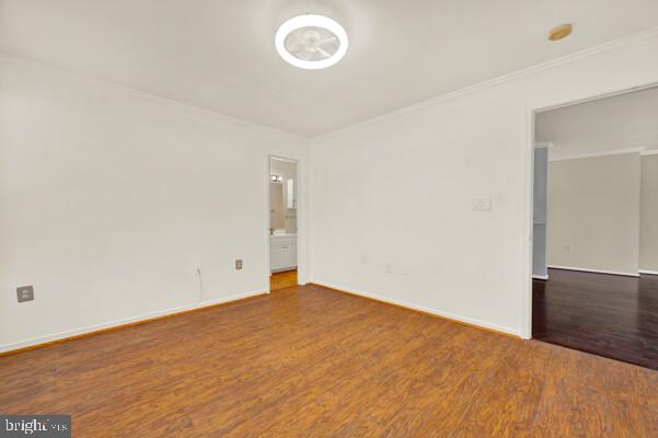 empty room with ornamental molding, wood finished floors, and baseboards