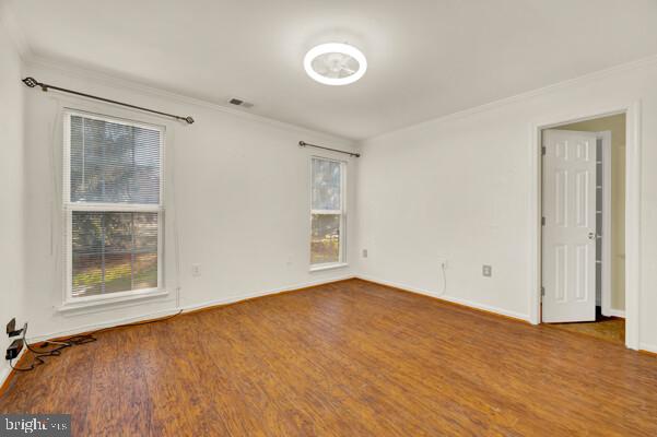 empty room with ornamental molding, a wealth of natural light, baseboards, and wood finished floors