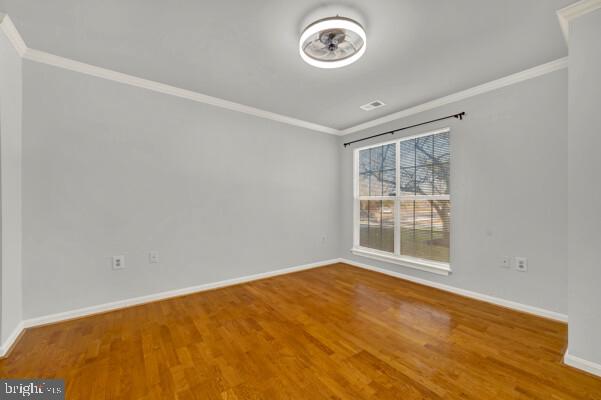 empty room with baseboards, wood finished floors, and crown molding