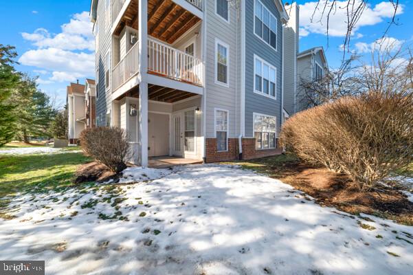 snow covered rear of property featuring brick siding and a balcony