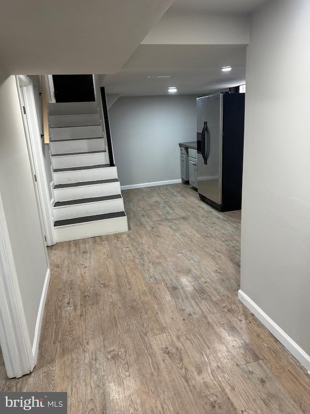 basement featuring stainless steel fridge with ice dispenser and light hardwood / wood-style floors