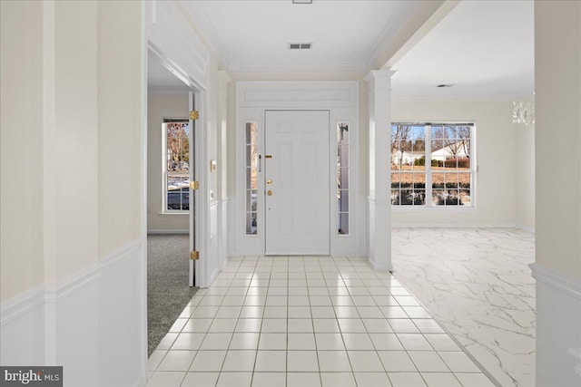 carpeted foyer entrance with crown molding, a healthy amount of sunlight, and ornate columns