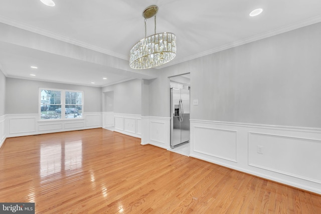 spare room with a notable chandelier, ornamental molding, and light wood-type flooring