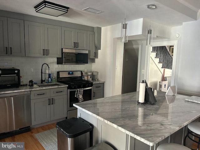 kitchen featuring stainless steel appliances, light stone countertops, sink, and gray cabinets