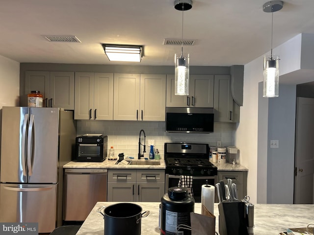 kitchen with sink, appliances with stainless steel finishes, gray cabinets, pendant lighting, and light stone countertops