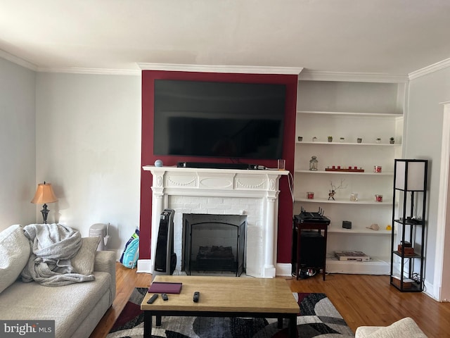 living room featuring crown molding, built in features, wood-type flooring, and a brick fireplace