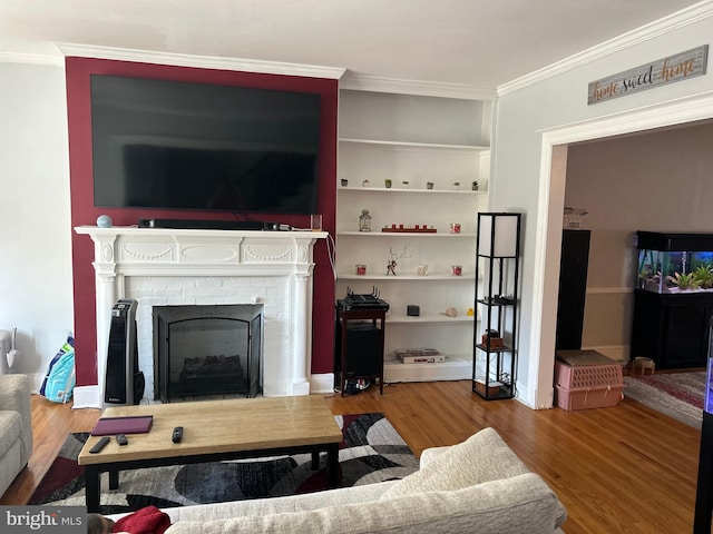 living room with a brick fireplace, crown molding, built in features, and hardwood / wood-style floors