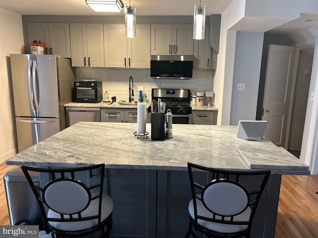 kitchen with wood-type flooring, gray cabinetry, hanging light fixtures, light stone counters, and stainless steel appliances