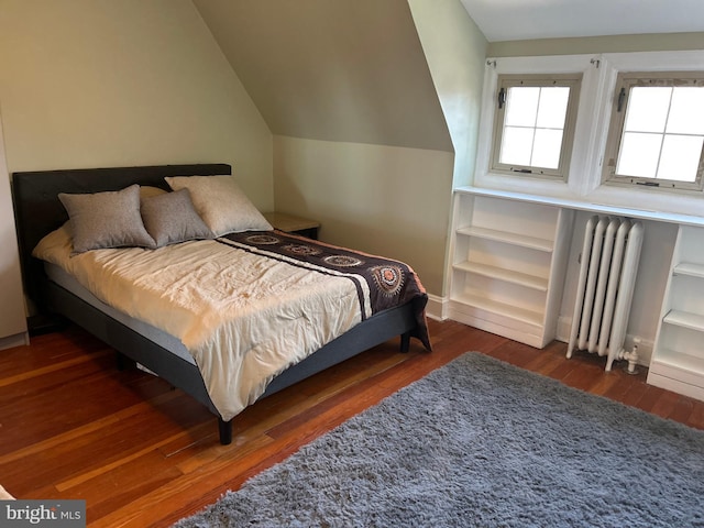 bedroom featuring dark wood-type flooring, radiator heating unit, and vaulted ceiling