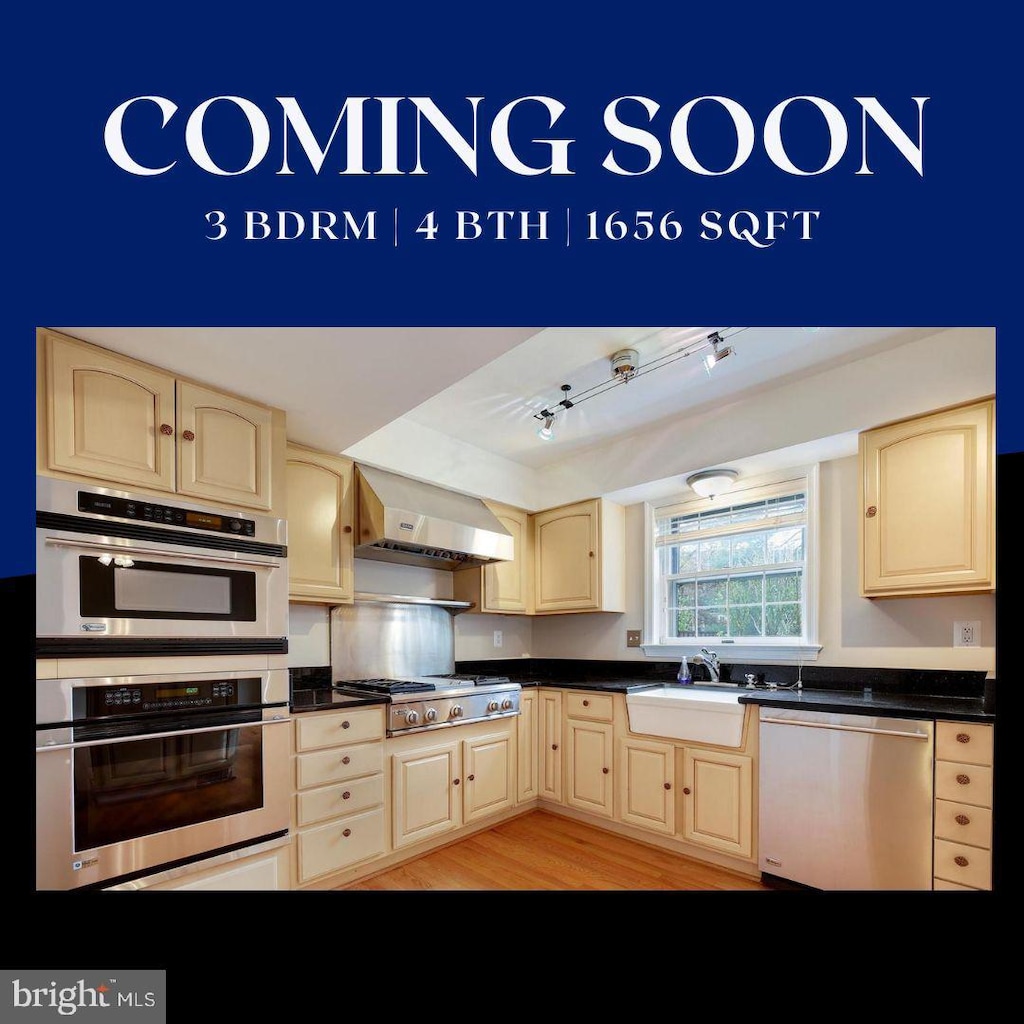 kitchen with stainless steel appliances, light brown cabinetry, sink, and wall chimney range hood