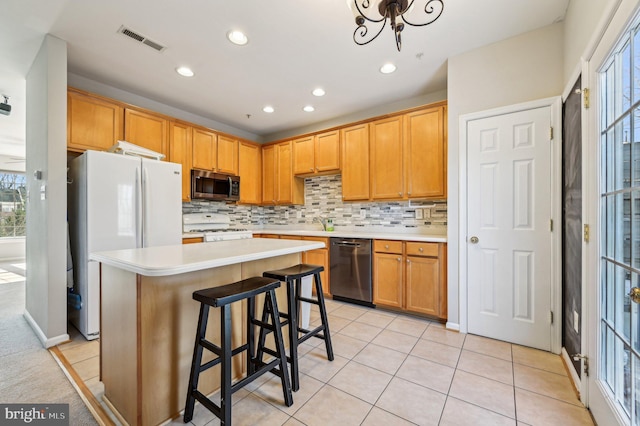 kitchen featuring a kitchen island, tasteful backsplash, a kitchen bar, light tile patterned floors, and white appliances