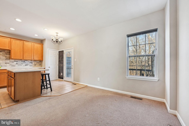 kitchen featuring a breakfast bar area, a center island, a notable chandelier, light carpet, and decorative backsplash